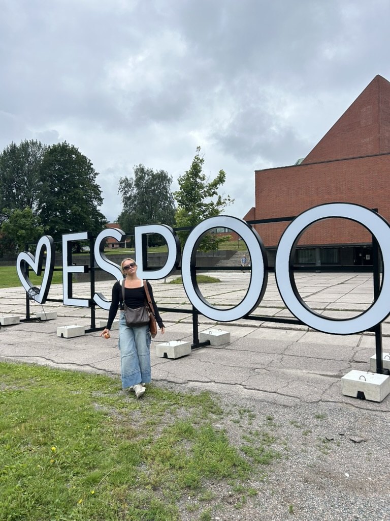 Standing in front of a large I love Espoo sign on a grey summer day.