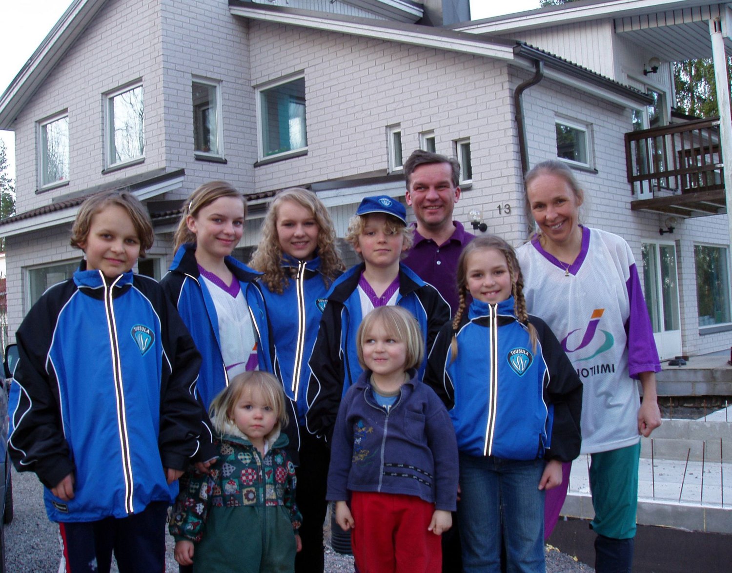 A family of nine outside a house, seven children and two parents, most of them in matching sports jackets.