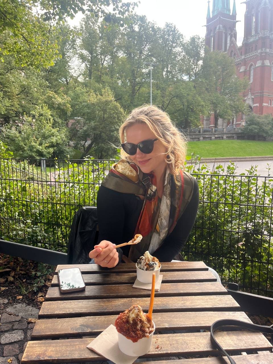Sitting at an outdoor table in Helsinki with two cups of ice cream, church spires behind.