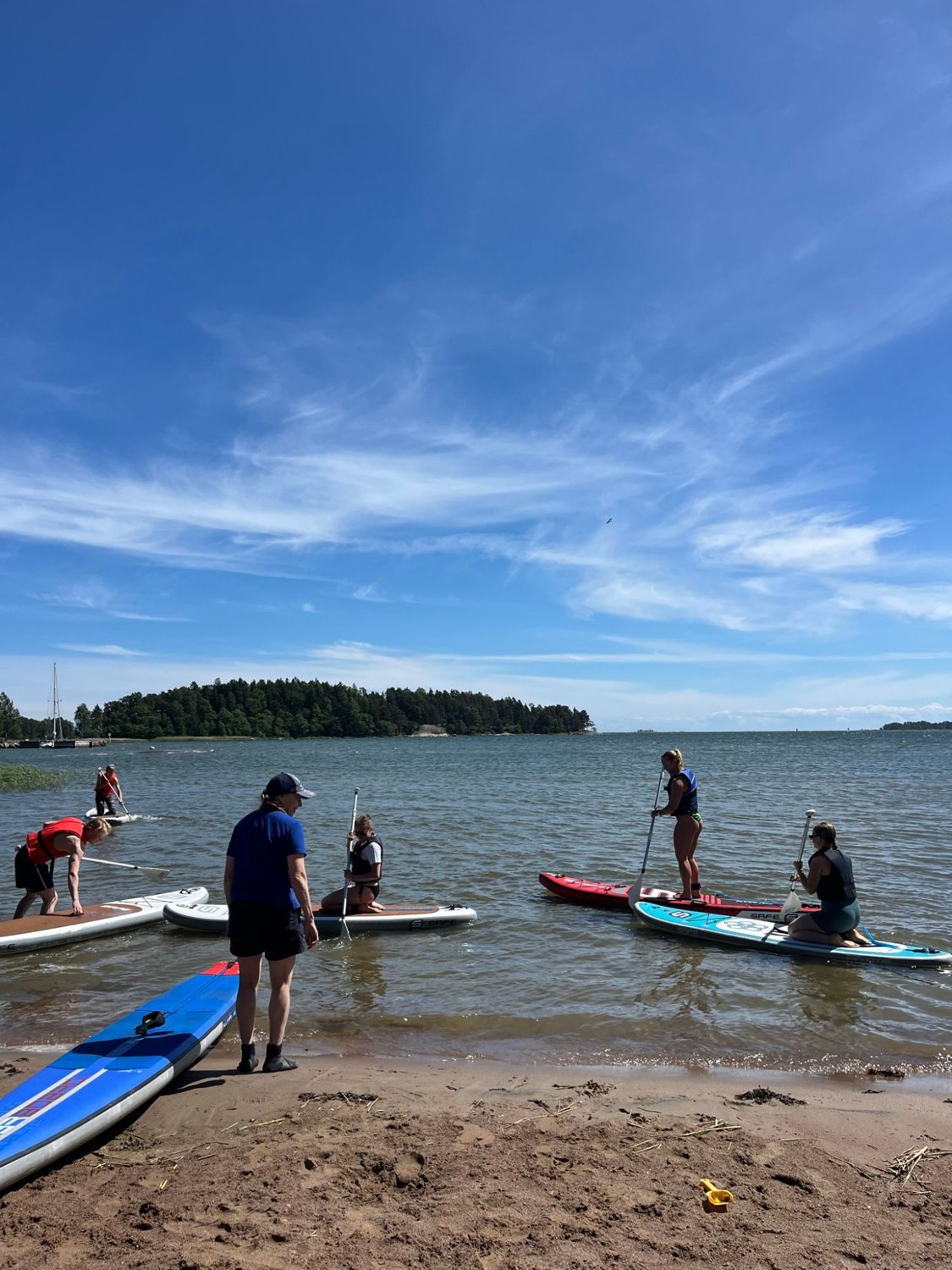 Mentors and mentees on paddleboards near the shore on a clear summer day.